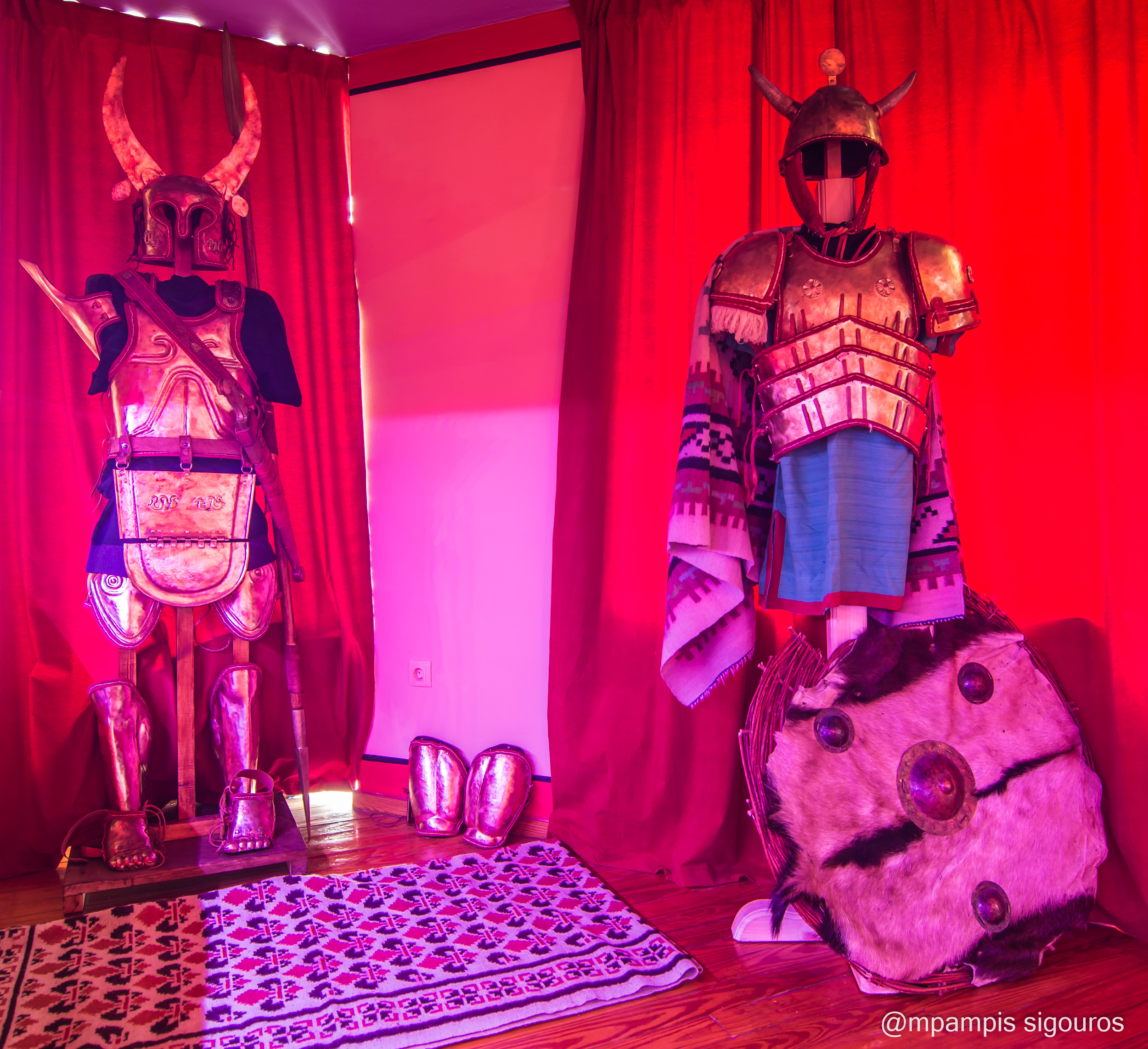Horned helmets and complete armour displays | Archaeopolis Atelier & Showroom Two complete reconstructed armour ensembles with horned helmets displayed against red curtains