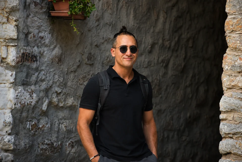 Georgios Katsos — Founder & Creative Director of Archaeopolis Georgios Katsos in a black polo shirt and sunglasses against a textured stone wall