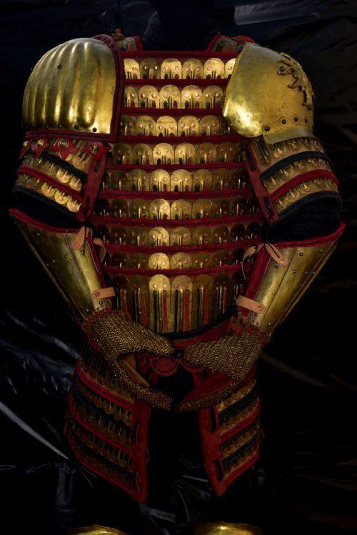 Reconstructed dark red and bronze lamellar armour displayed against a black background