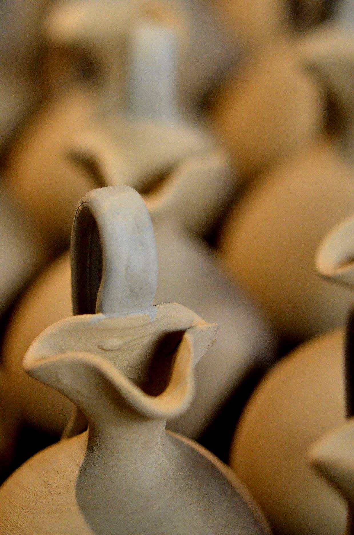 Close detail of a small handmade clay pouring vessel with a tall handle and pinched spout
