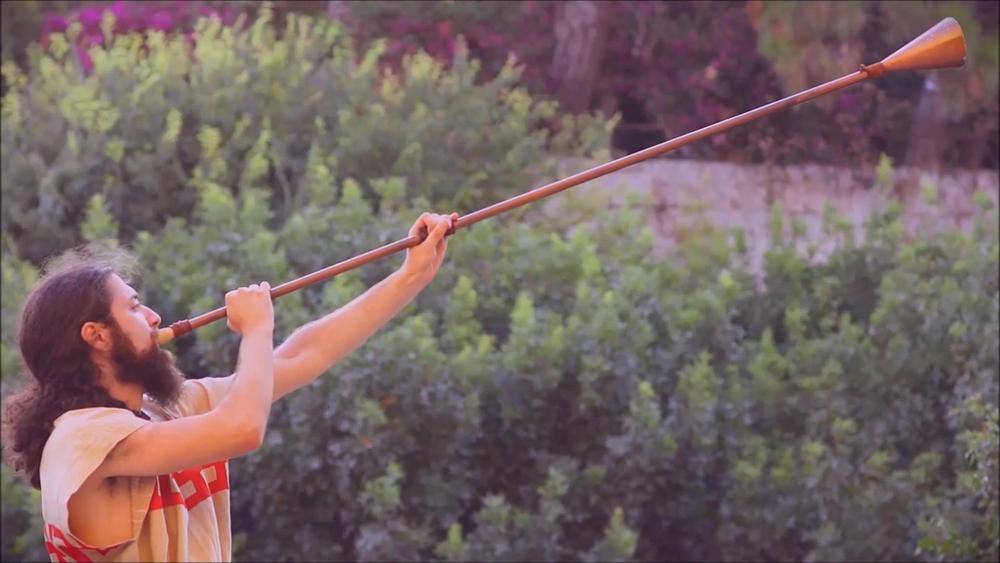 Male performer playing a long reconstructed trumpet outdoors
