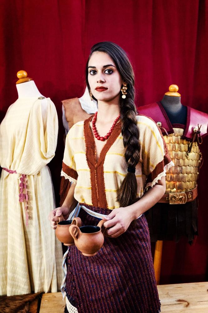 Female historical interpreter standing beside displayed costumes and armour