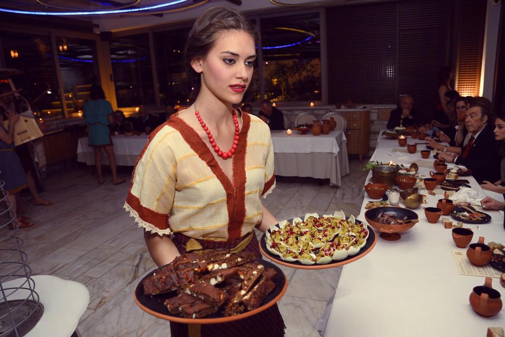 Costumed woman presenting prepared dishes at a reconstructed historical banquet