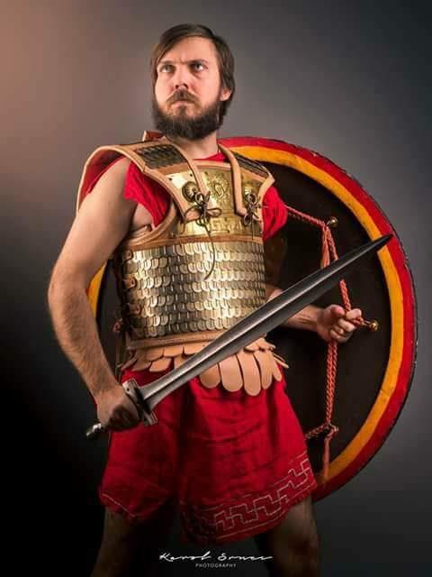 Bearded hoplite posed in bronze armour with a red round shield and spear