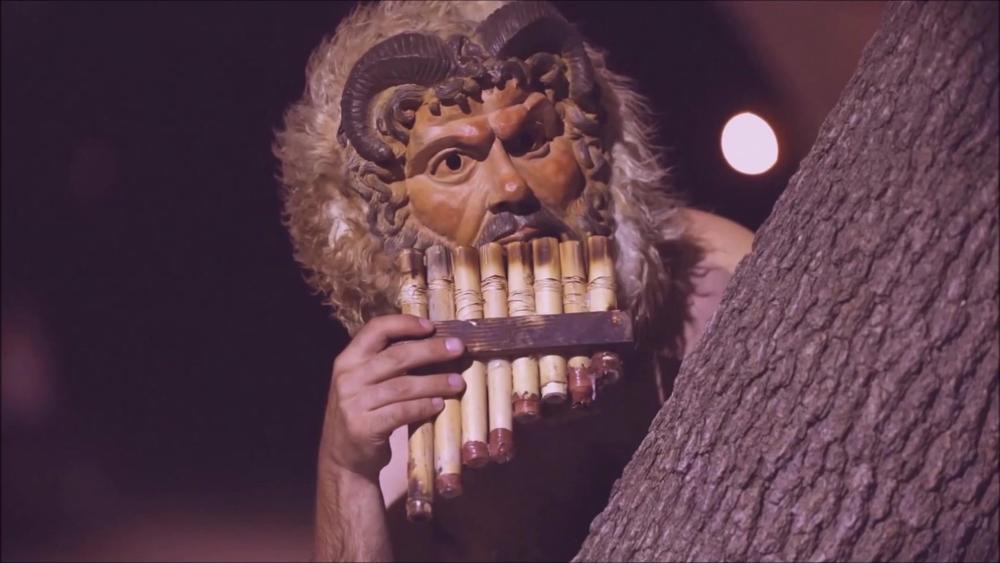 Performer wearing a Pan mask and playing pipes during an outdoor night performance