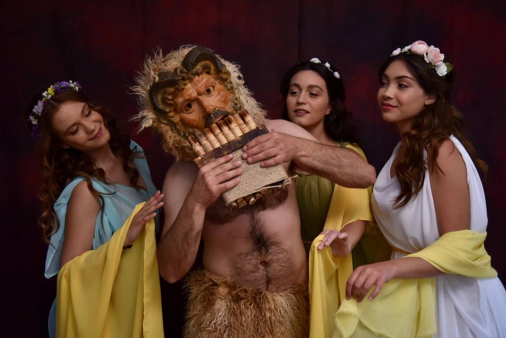Pan character surrounded by three women in floral crowns and draped costumes