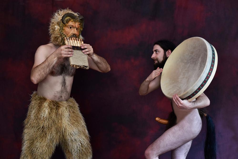 Two performers portraying Pan figures with pipes and a large frame drum