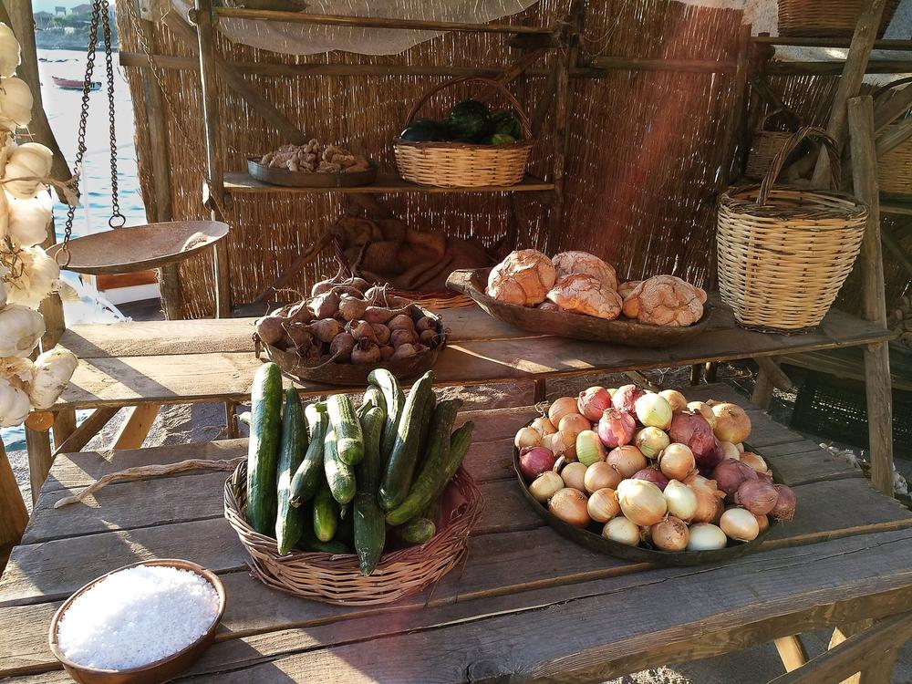 Historical vegetable stall with cucumbers, onions, garlic and pottery bowls