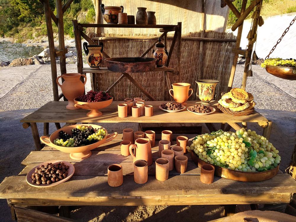 Historical food and wine display with grapes, fruit, pottery cups and amphorae