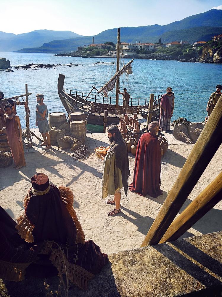 Costumed historical interpreters gathered beside a reconstructed ancient vessel at the waterfront