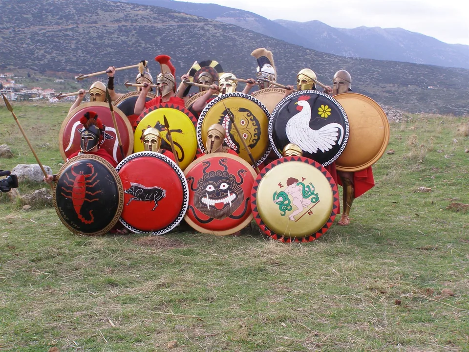 Group of hoplite reenactors holding decorated round shields and spears outdoors