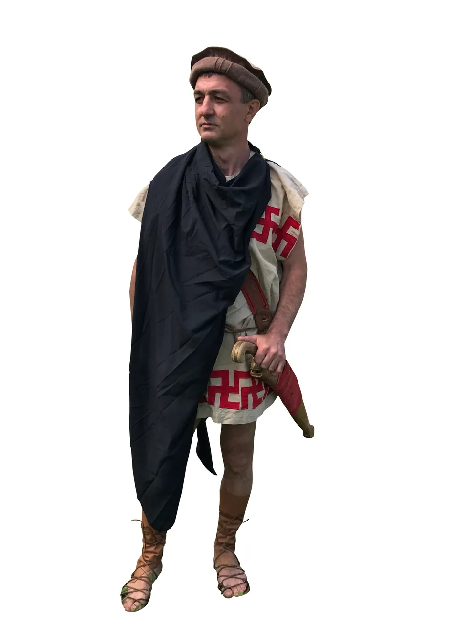 Full-length costume portrait of a man wearing a brown cap, cream tunic with red geometric motifs, dark draped cloak and laced leather footwear, with a sheathed sword