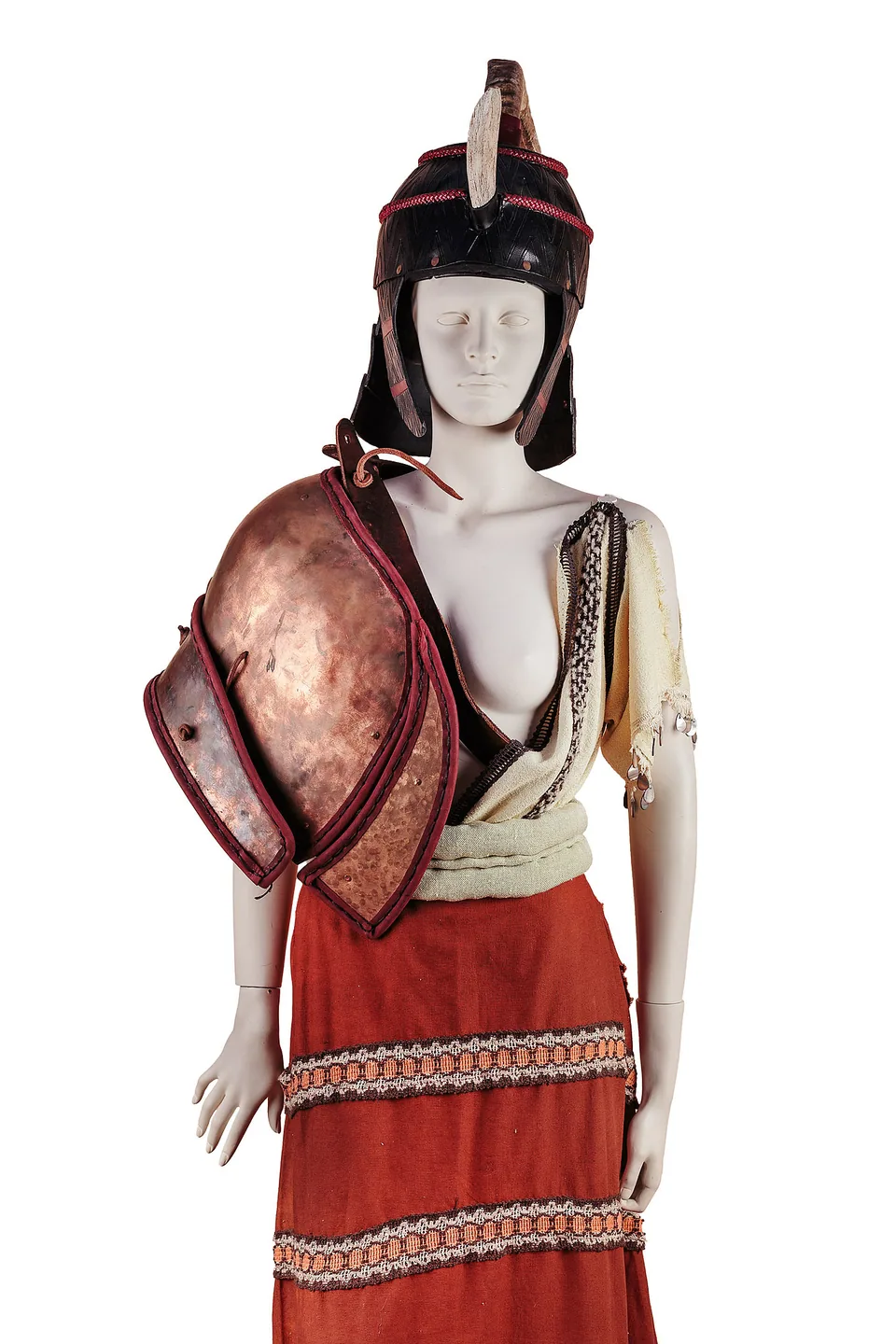 Costume on a mannequin with a Mycenaean-style dark horned helmet, copper-coloured shoulder armour, cream draping and a red woven skirt