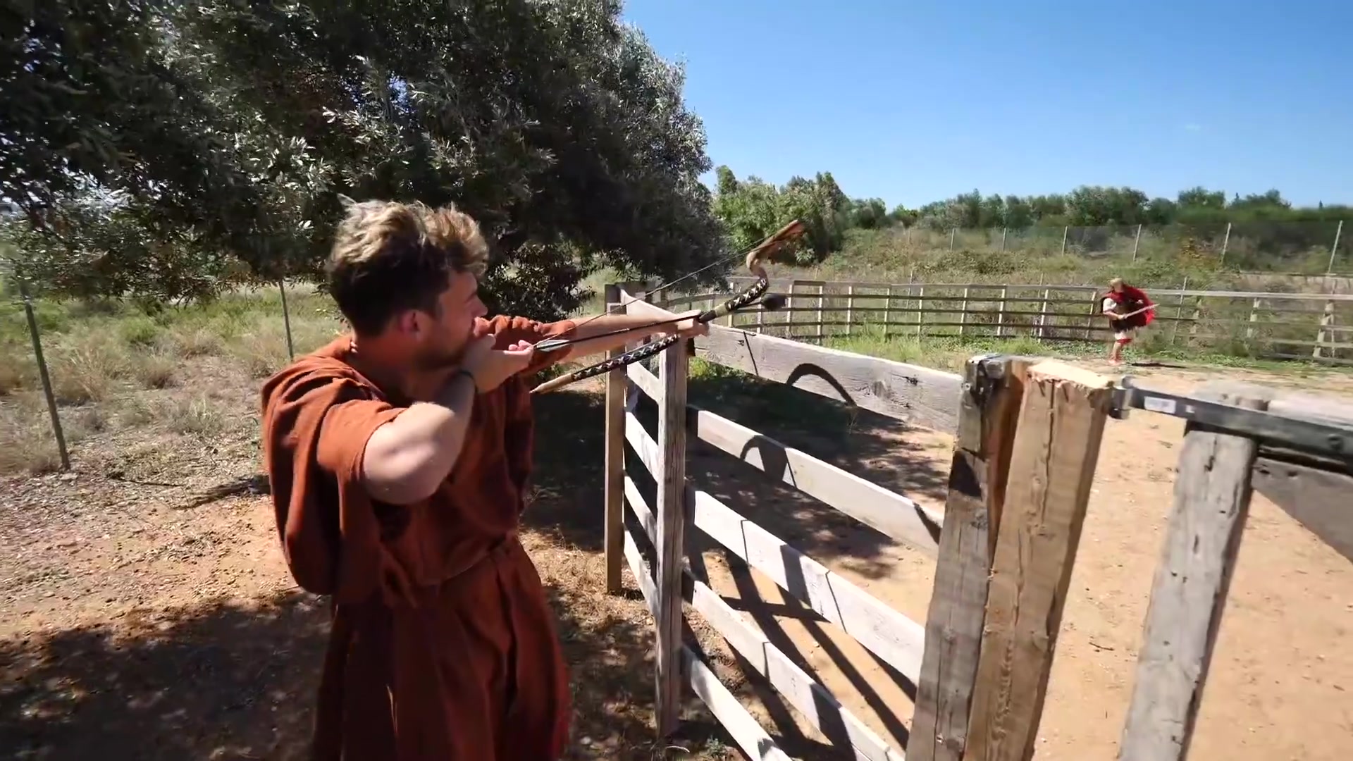 Supervised participant at the shooting line | Archaeopolis Archery Games Young participant aiming a bow from behind a wooden barrier