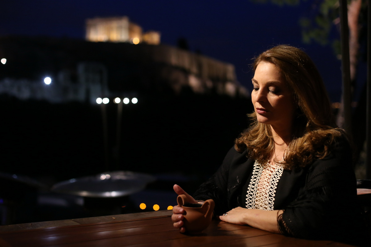 A woman holding a terracotta cup at the private dinner at Dionysos Zonar’s, with the illuminated Acropolis in the background