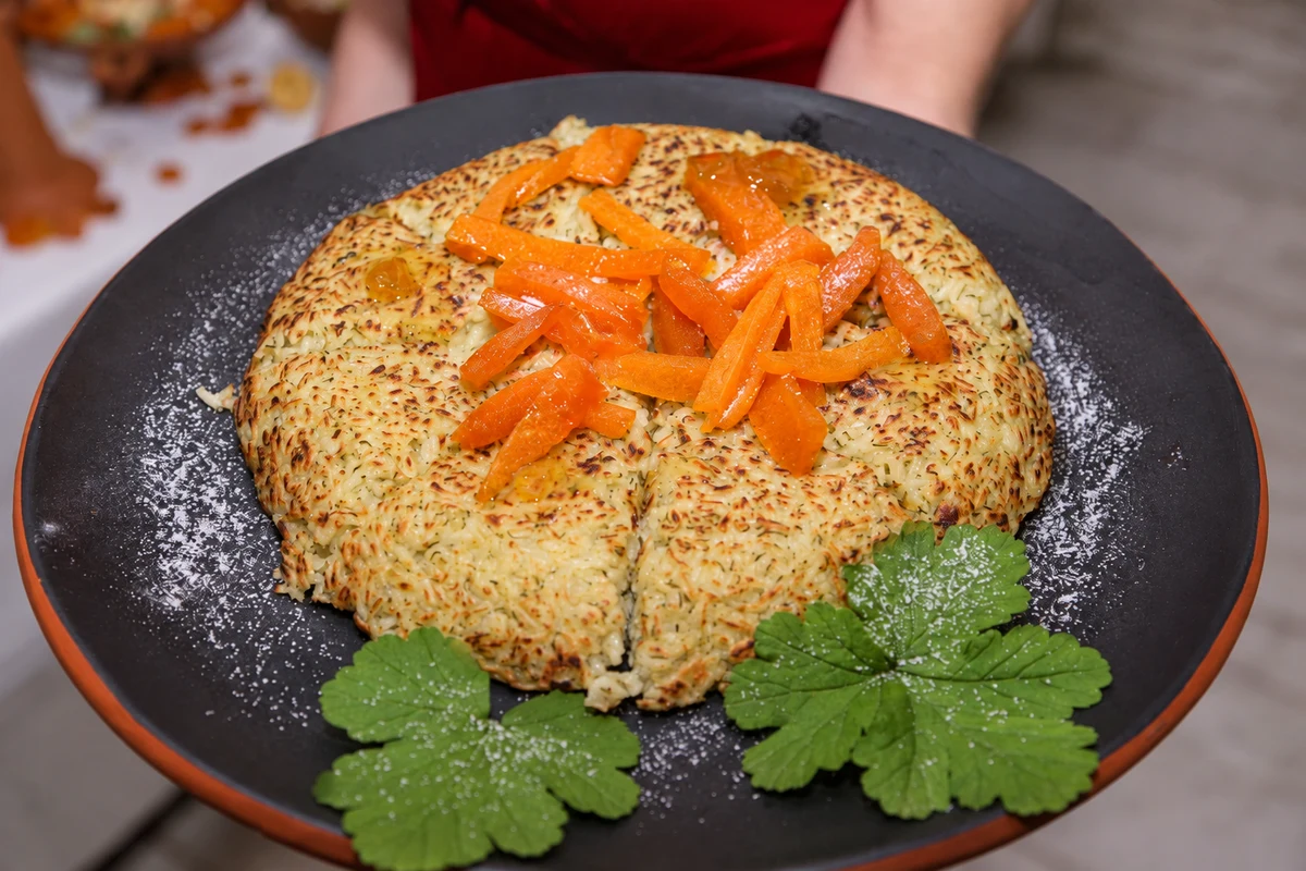 Rice pie with orange-coloured garnish and green leaves on a dark serving platter.