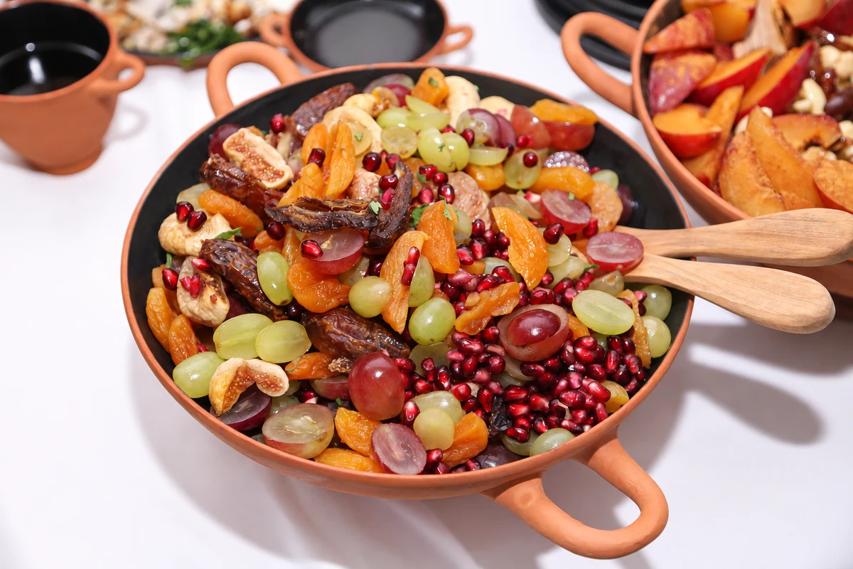 Fruit salad in a terracotta bowl with wooden serving utensils.