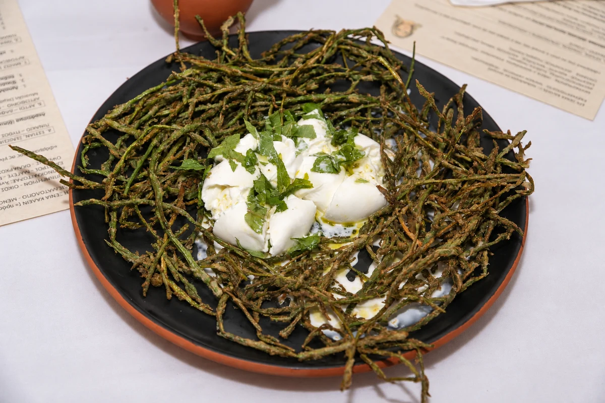 Green vegetable stems surrounding soft white portions with chopped herbs on a dark plate.
