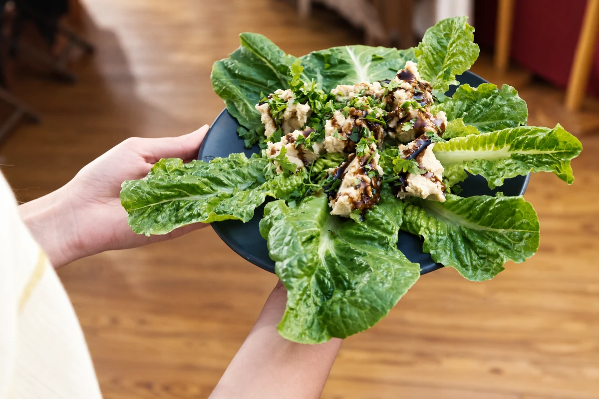 A dark platter with lettuce leaves, pale portions, herbs and a dark dressing, held for serving.
