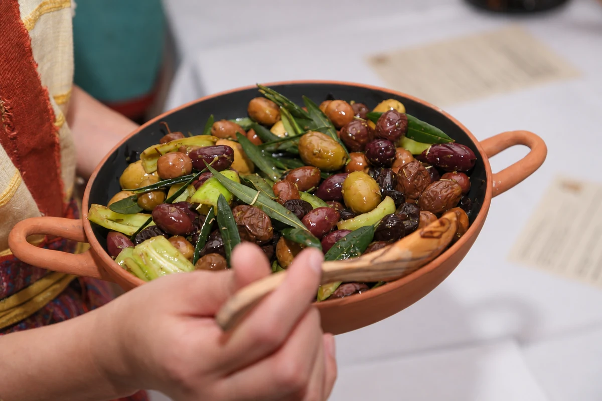 Mixed olives with green leaves in a terracotta serving bowl.
