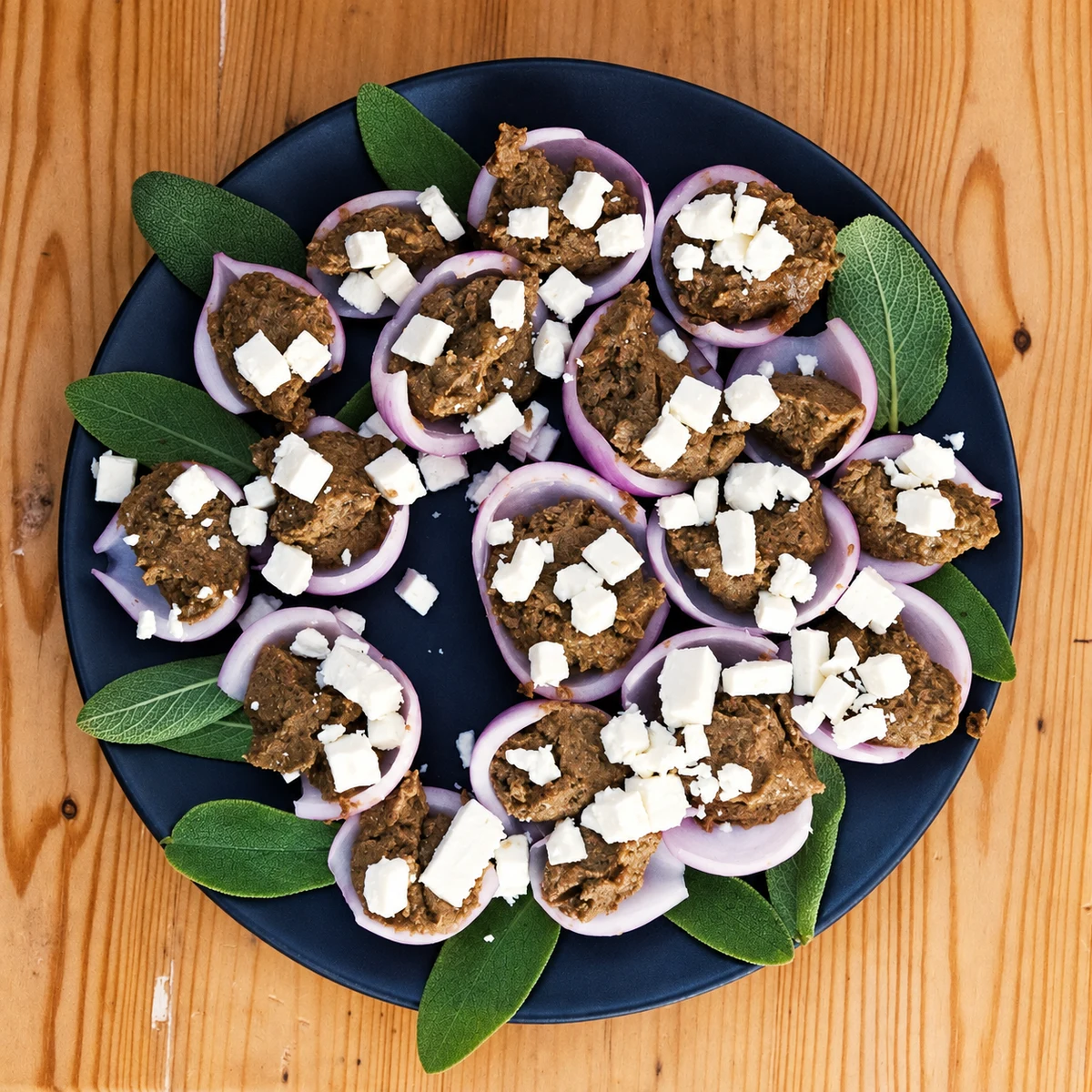 Onion petals with a dark filling and white cheese pieces, arranged with green leaves on a dark plate.