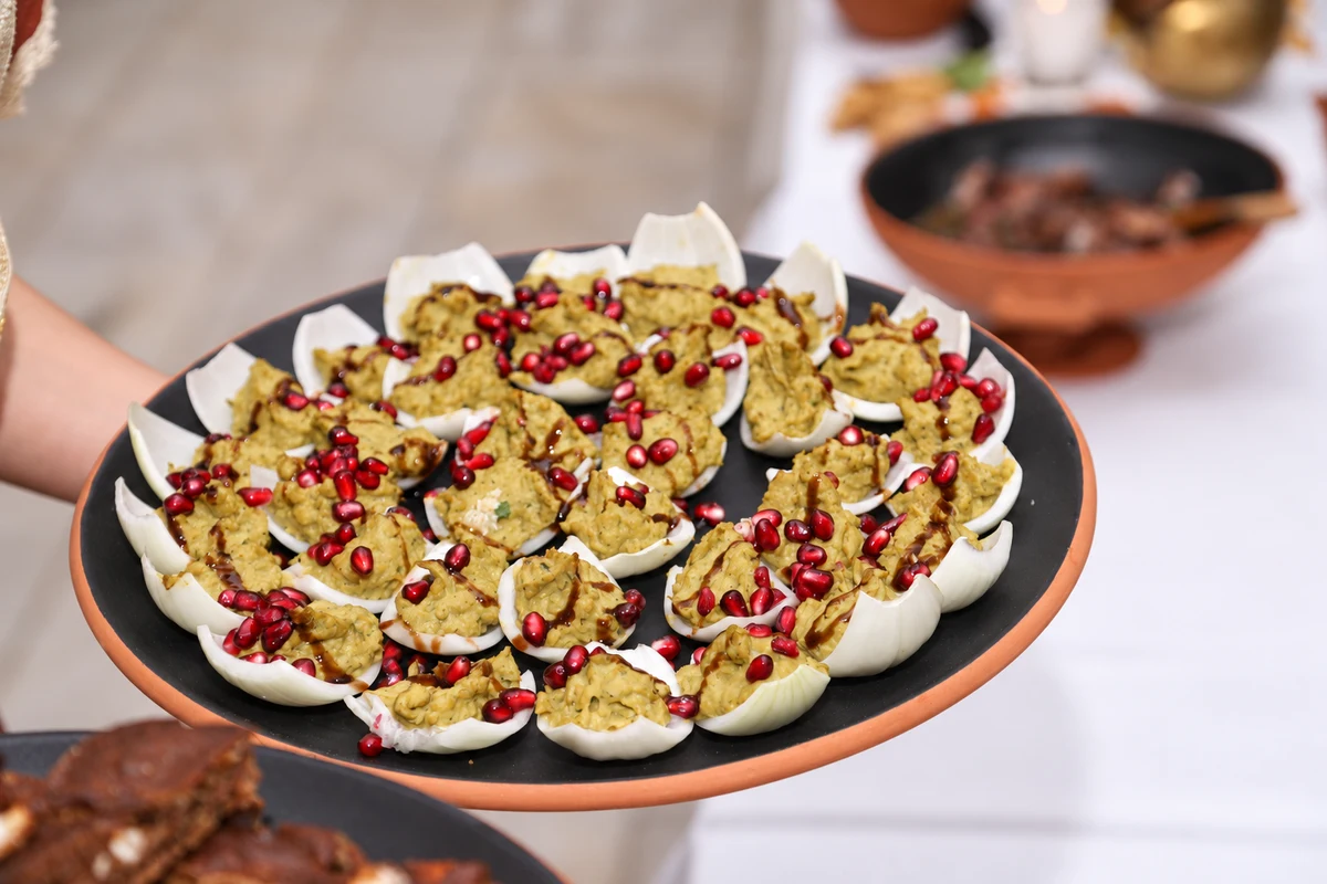 Filled onion petals with pomegranate seeds and a dark dressing on a serving platter.