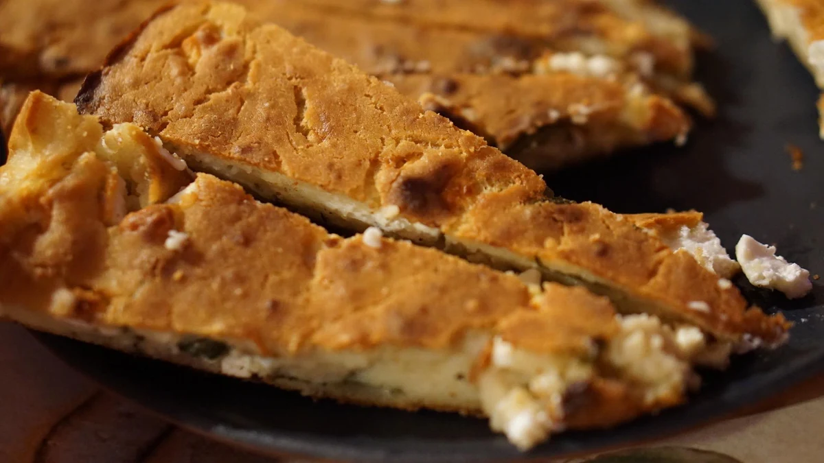 Golden baked pie cut into slices on a dark serving plate.