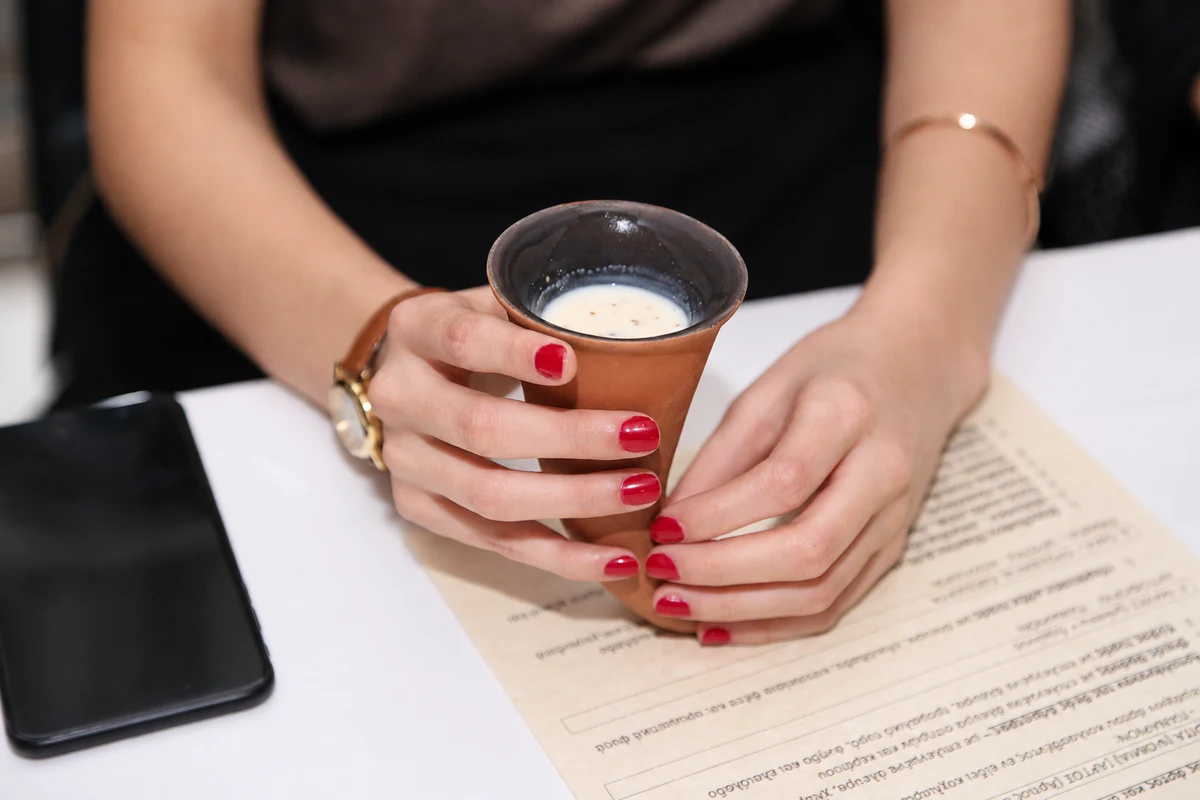 Hands holding a terracotta cup containing a pale drink above a printed menu.