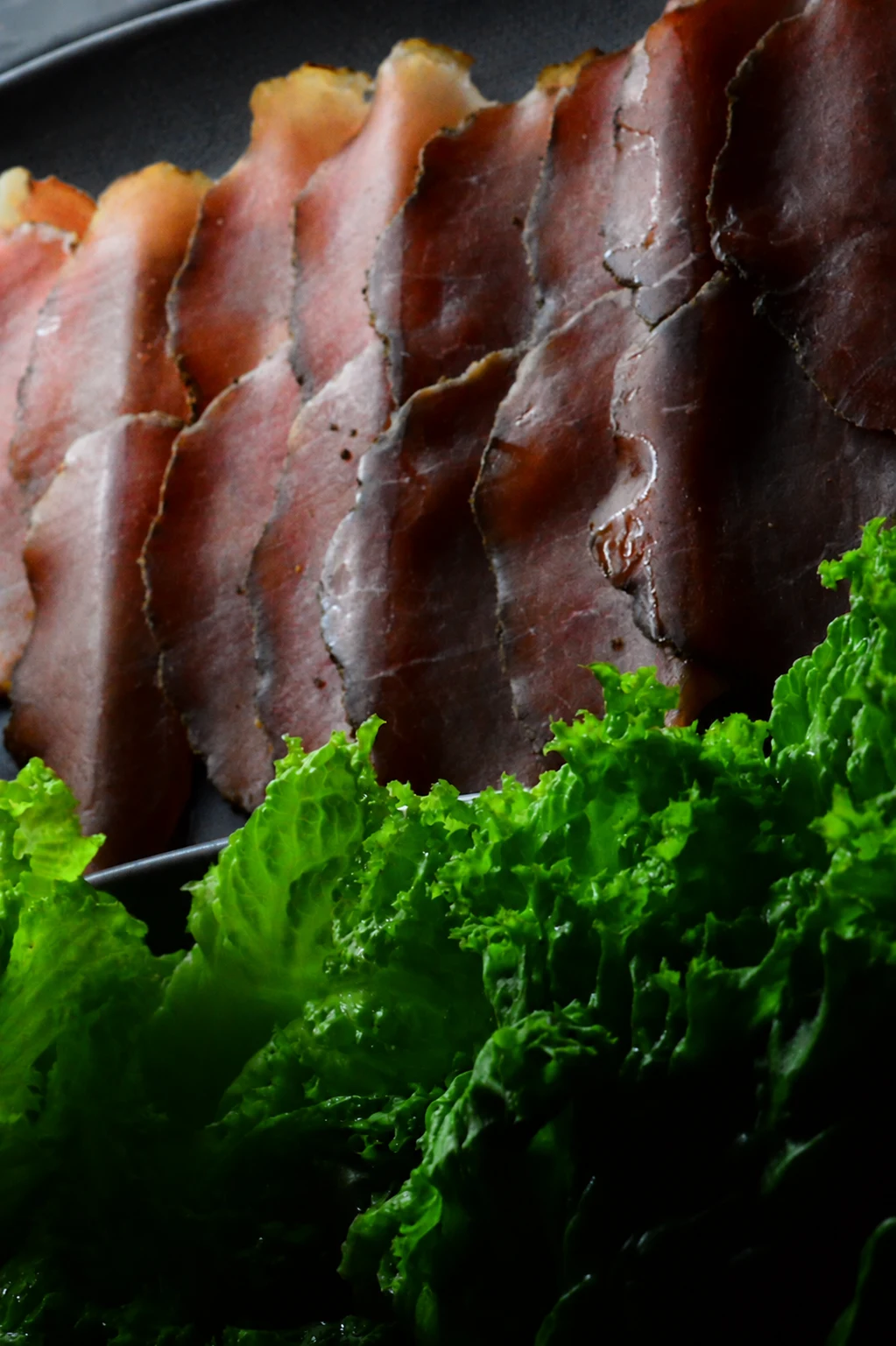 Slices of meat with green lettuce on a black serving plate.
