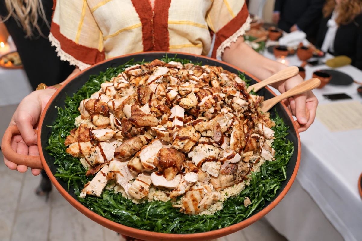 Sliced cooked poultry over grains and greens on a large terracotta platter.