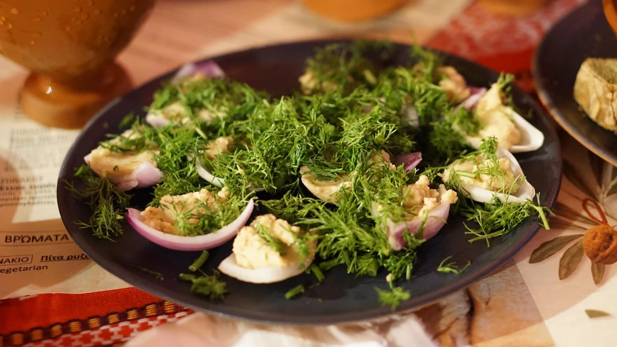 Small appetisers served in onion petals with chopped green herbs on a dark plate.