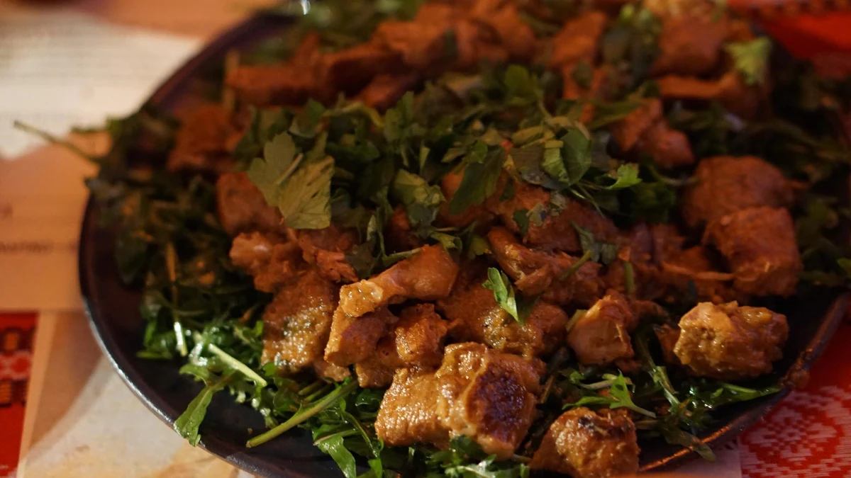 Browned pieces of meat served over leafy greens on a dark platter.