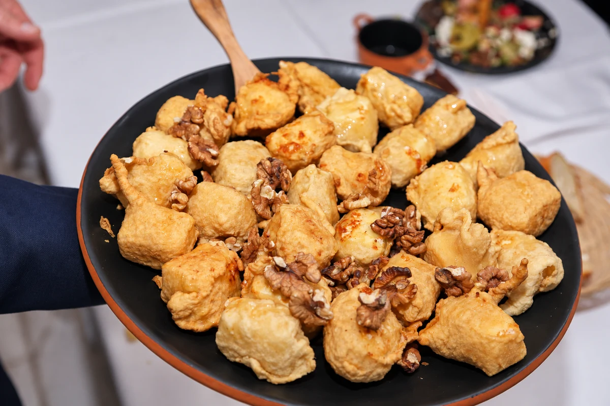 Golden pastries with walnuts and a glossy drizzle on a dark serving plate.