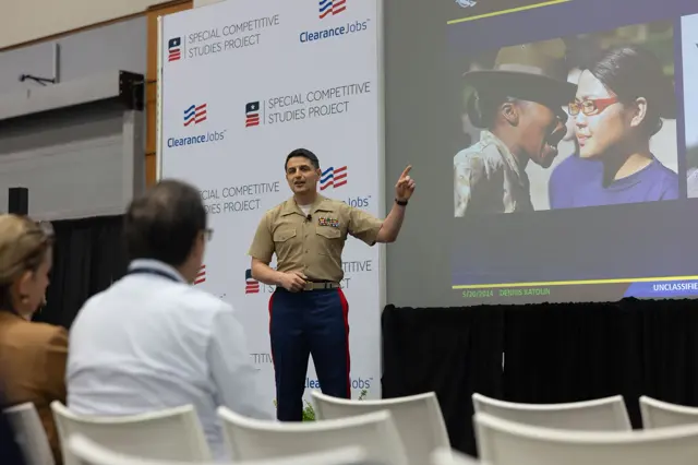 Speaker addressing attendees beside a large presentation screen at the AI+ Expo in Washington DC