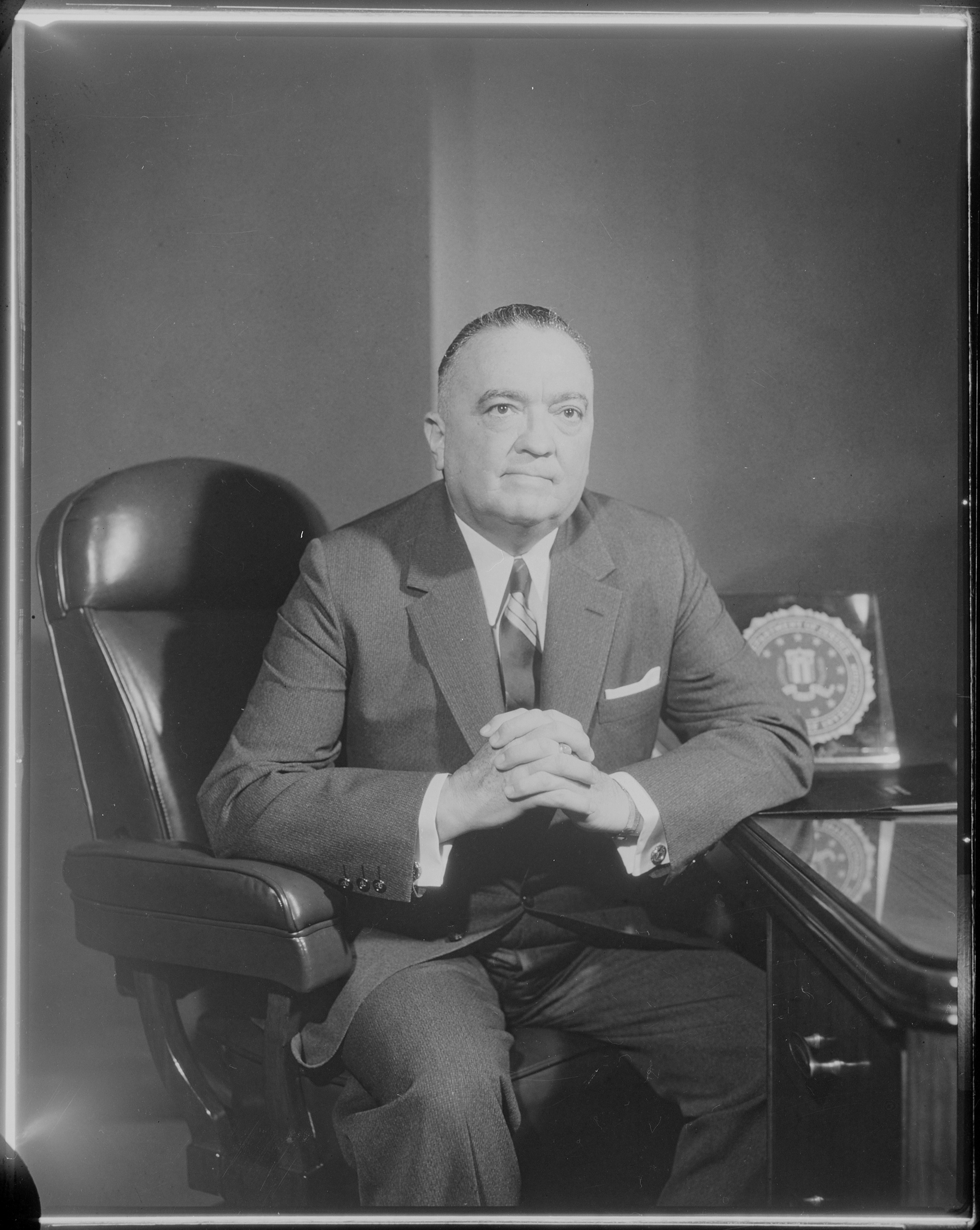 J. Edgar Hoover and the machinery of the FBI Black and white archival portrait of FBI Director J. Edgar Hoover seated at his desk