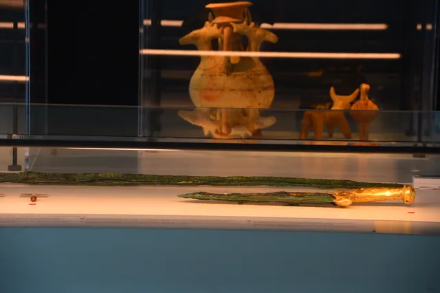 Two long metal blades displayed in front of an animal-shaped vessel and small clay figurines.