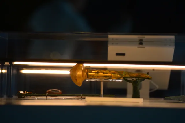 Long ancient metal objects, including a blade with a gold-coloured section, displayed horizontally.