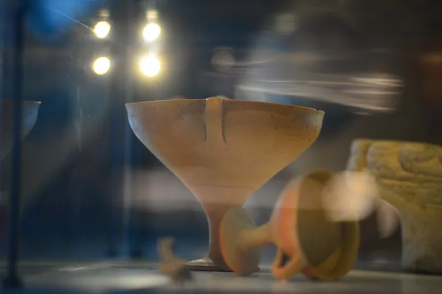 Pale ceramic stemmed cup displayed behind glass.