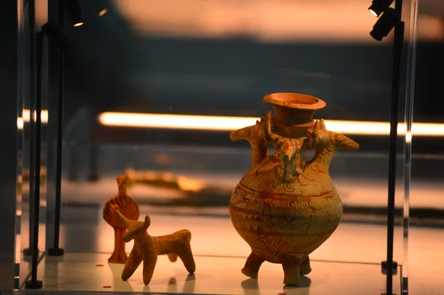 Painted animal-shaped ceramic vessel displayed beside small clay animal figurines.
