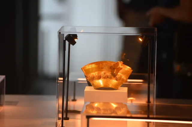 Shallow gold vessel with spiral relief decoration illuminated against a dark background.