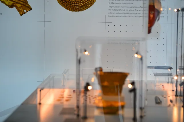 Museum cases containing gold vessels and small artefacts beside an explanation of goldworking techniques.