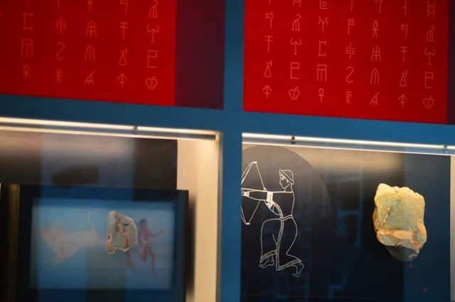 Exhibition display with red Linear B sign graphics above fragments of a painted human figure.