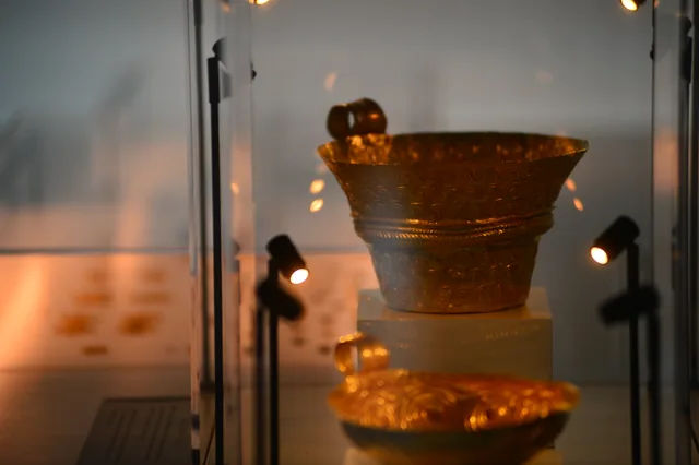 Close-up of two decorated gold vessels arranged vertically in a museum case.