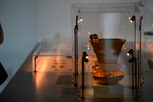 Two decorated gold vessels illuminated inside a museum display case.
