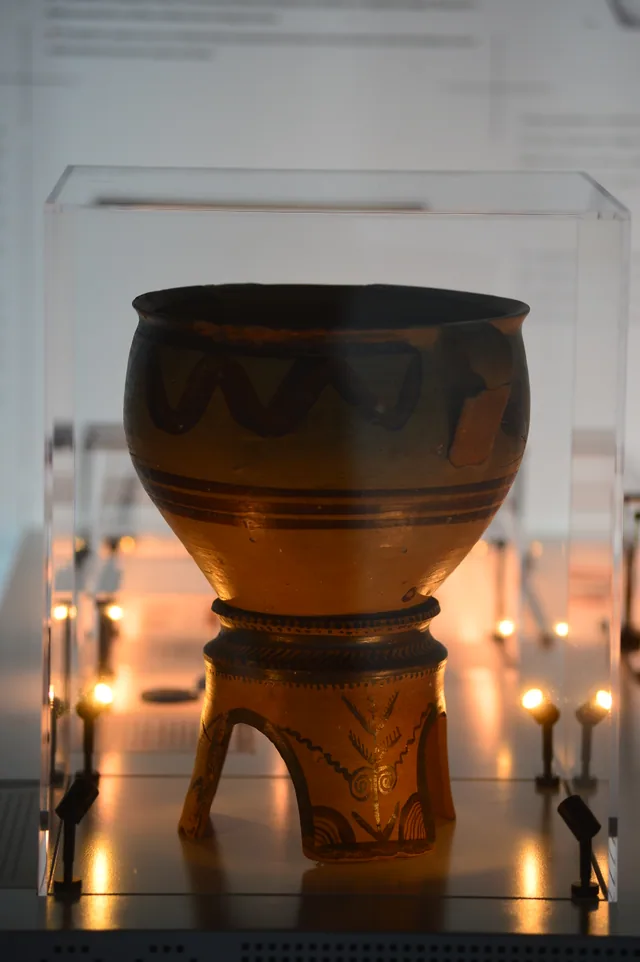 Large painted clay vessel with dark wave patterns on a decorated tripod stand.