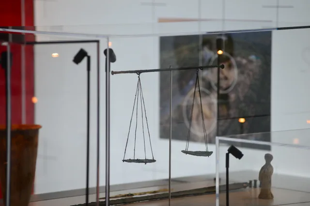 Suspended two-pan balance scale displayed inside a museum case.