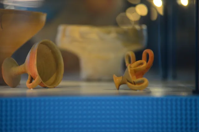 Two small clay vessels, including a tilted cup and a pot with circular handles.