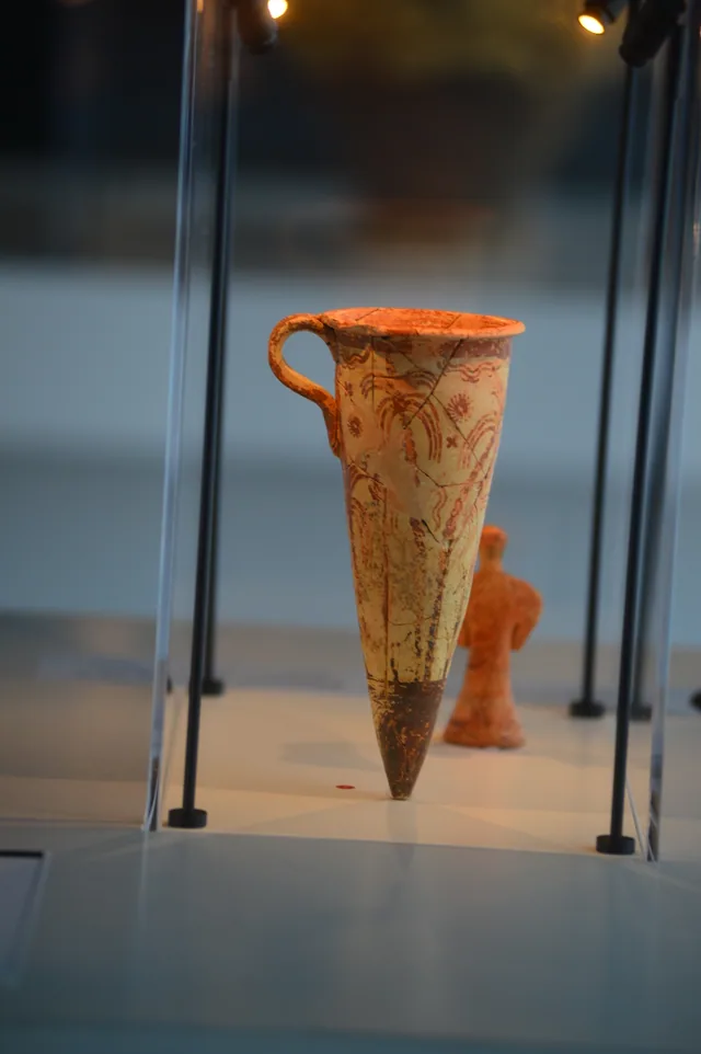 Tall narrow painted ceramic vessel with one handle and a pointed base.