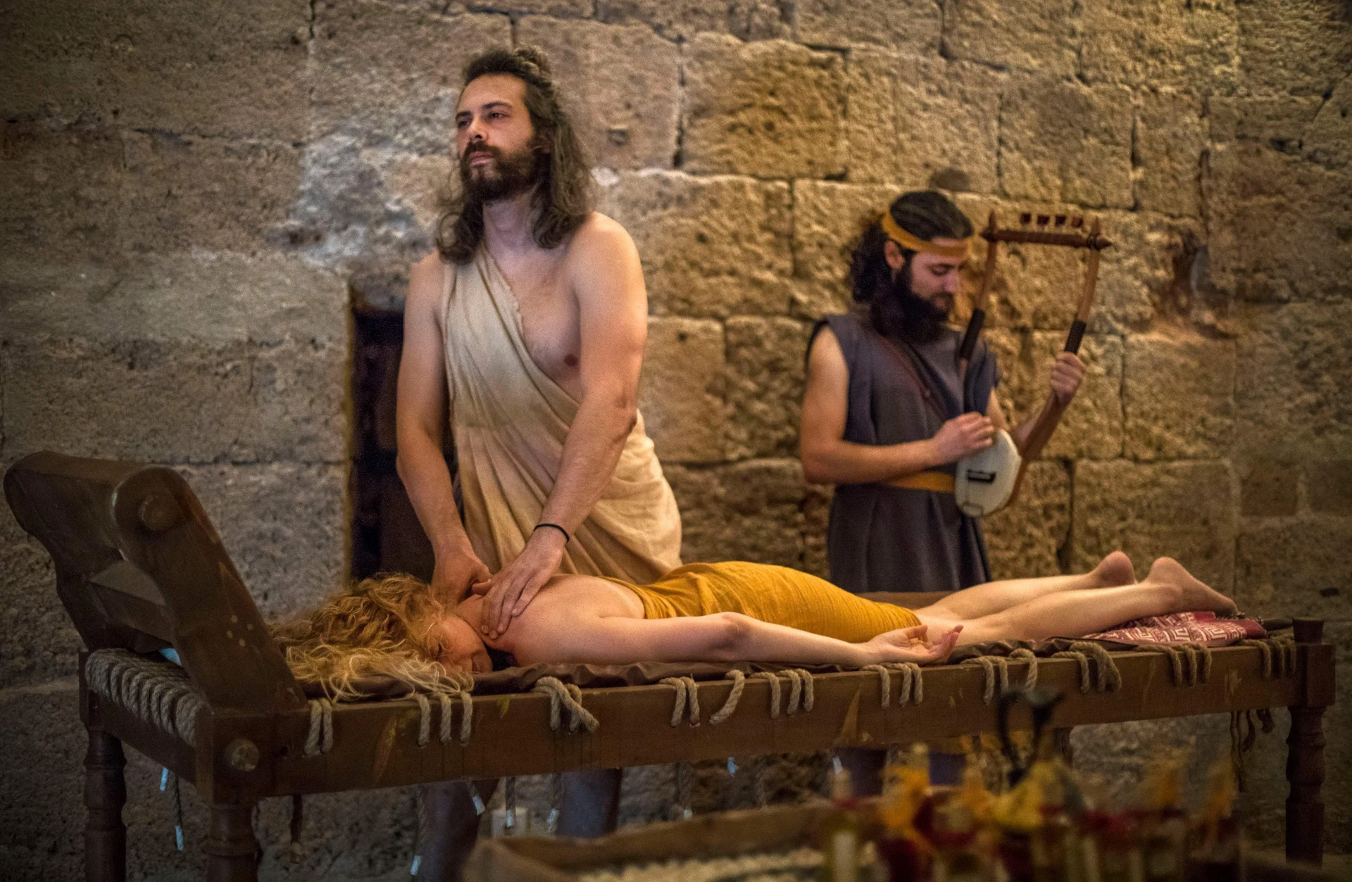 Massage demonstration on a reconstructed couch with a lyre player beside the participant
