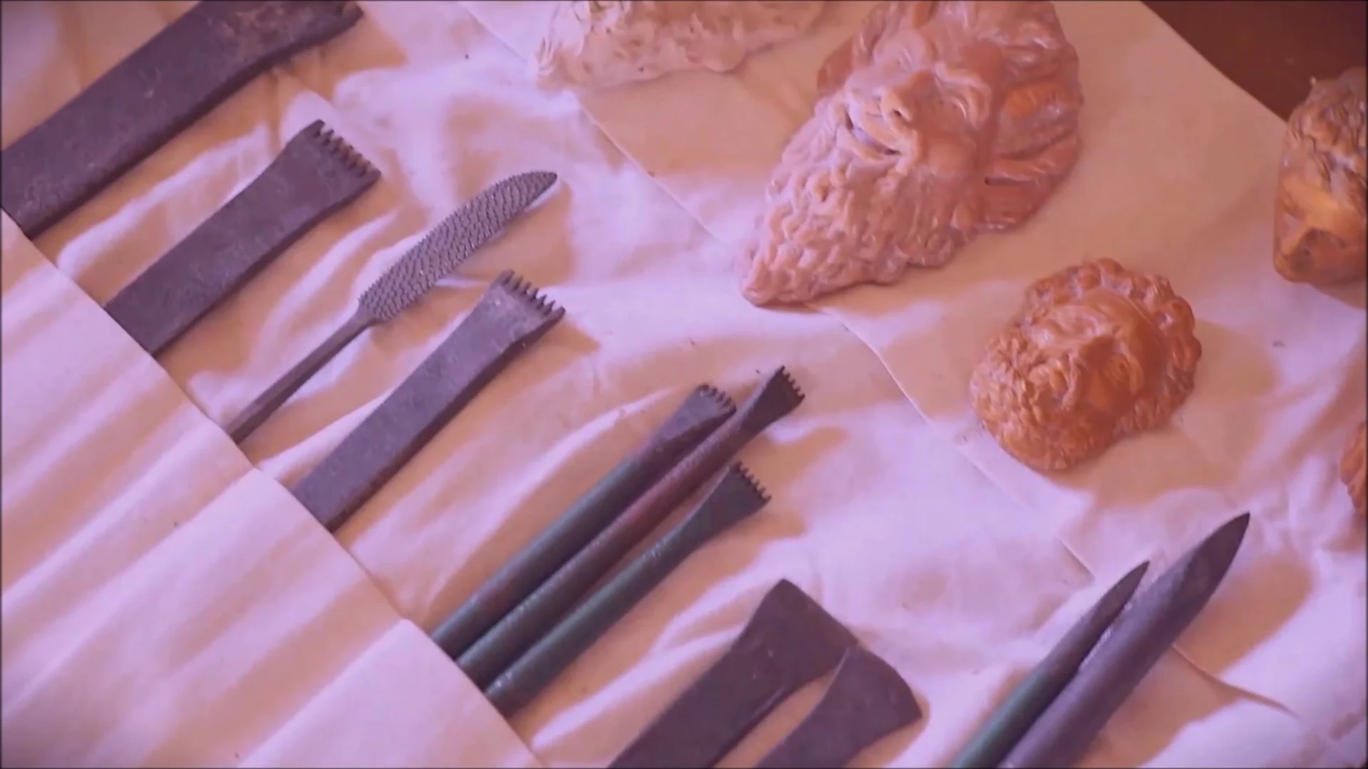 Sculpting tools arranged beside small sculpted heads on a fabric-covered display